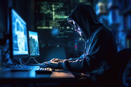 Hacker sitzt im Hoodie am Rechner.